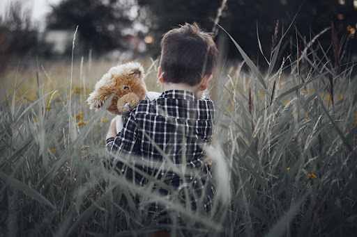 child sitting in field with teddy bear