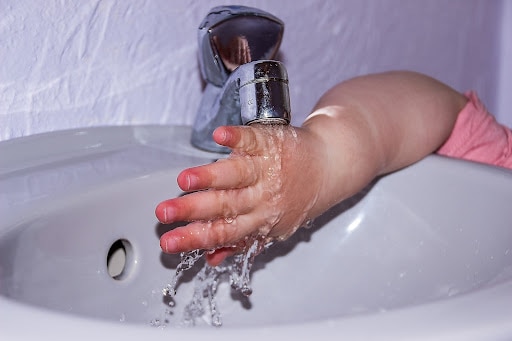 child hand under water faucet with water running