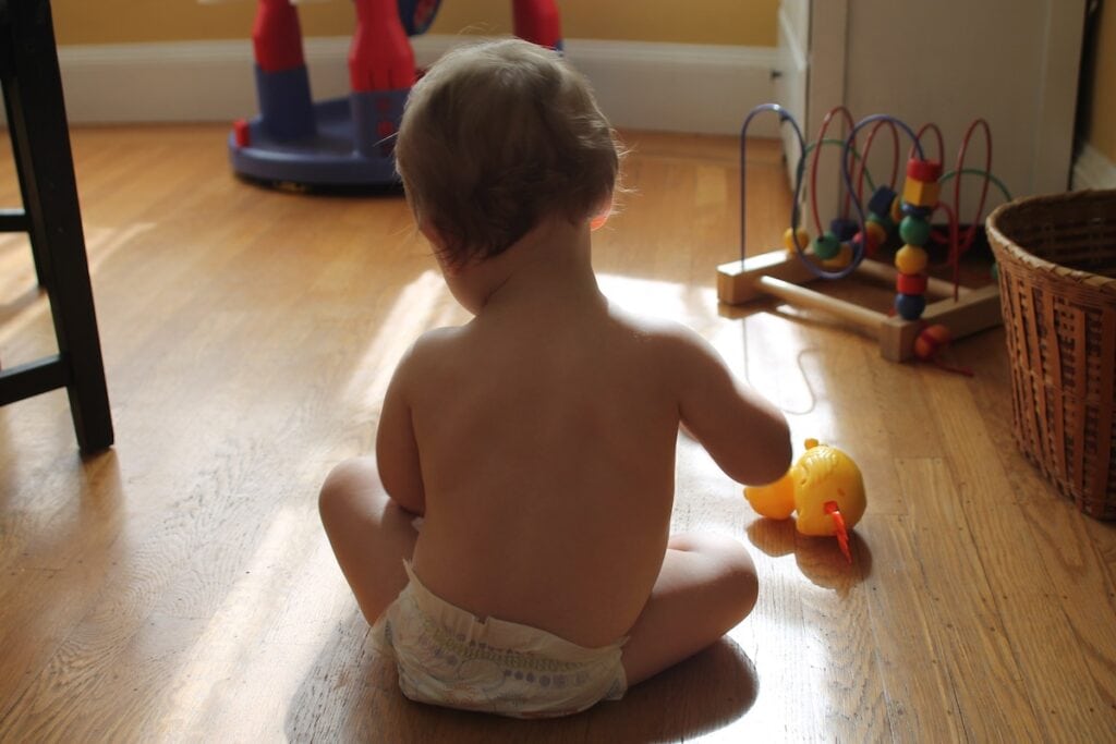 child in diaper sitting on floor playing with toy